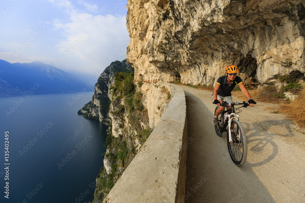 Mountain biking at sunrise woman over Lake Garda on path Sentier