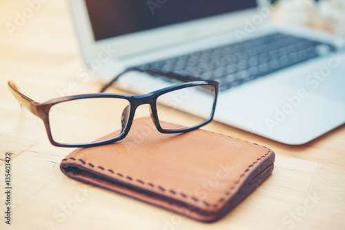 glasses on wallet and laptop on wooden table