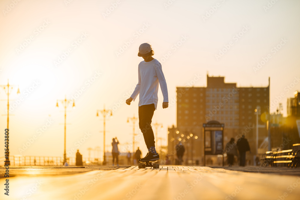 Young skaterboy riding longboard on the boardwalk, silhouette on sunset Young skaterboy riding longboard on the boardwalk, silhouette on sunset