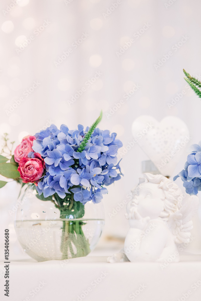 Bowl with blue hydrangeas and pink roses stands behind statue of Bowl with blue hydrangeas and pink roses stands behind statue of