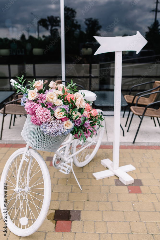Decorative white bicycle with basket and flowers stands in the r