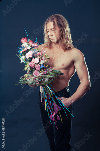 manly muscular man with long hair holds in hands a bouquet of flowers design