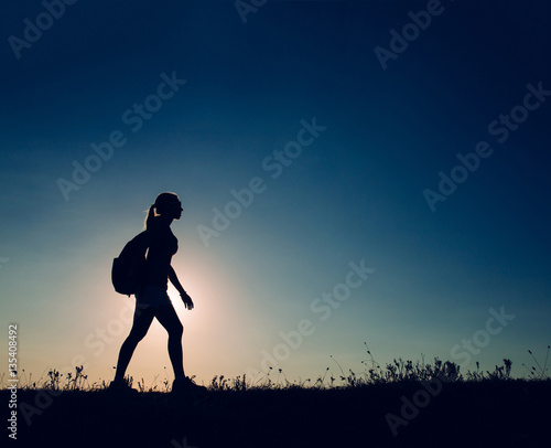 silhouette Young woman tourist with backpack goes on the background on sunset sky