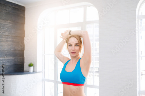 Young woman stretching near big windows with earphones at home