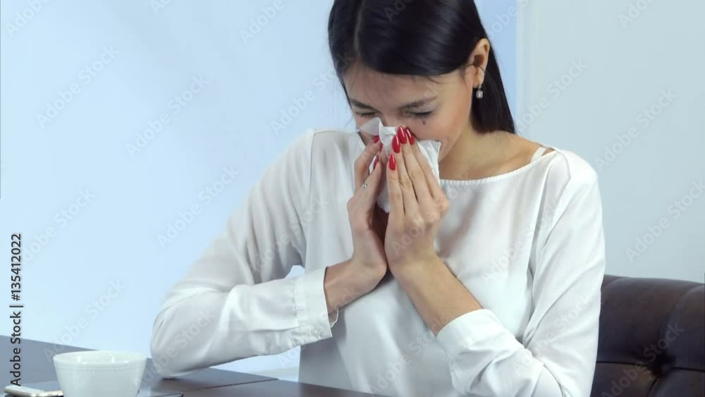 Sick business woman sneezing and blowing her nose while signing papers in a cafe Sick business woman sneezing and blowing her nose while signing papers in a cafe