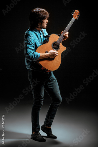 Cool guy standing with guitar on dark background