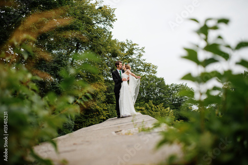 Embracing wedding couple in love on cloudy weather outdoor.