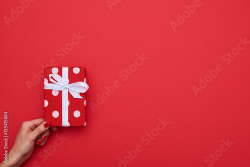 Woman holding a gift box with one hand isolated over red backgro