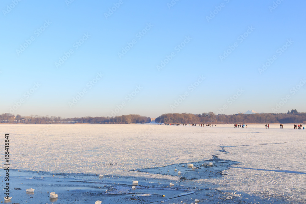 People walking and ice skating on partly frozen Lake Chiemsee