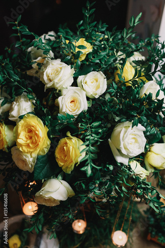 Bouquet of dark greenery and white roses with candles hanging fr © myronovychoksana