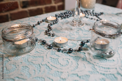 Little white candles stand along chain of pearls on blue table
