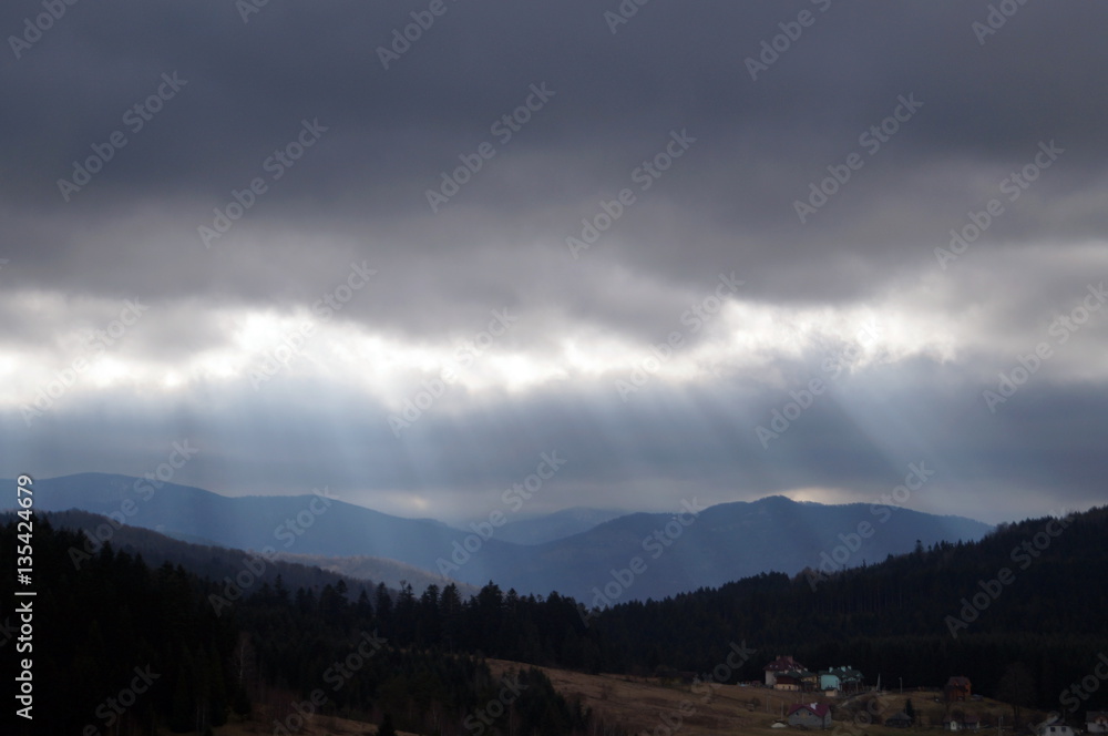 Mountain View covered with green forest in the rays of the sun that is falling from the cloudy sky dark