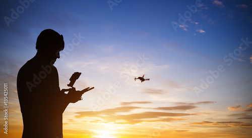 Fotografie, Tablou Drone pilot with quadrocopter. Silhouette against the sunset sky