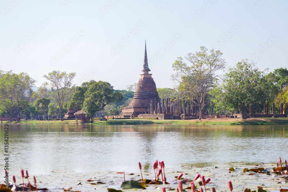Obraz premium Ancient buddha statue and pagoda with lotus in the pool at Sukhothai Historical Park, Sukhothai Province, Thailand.