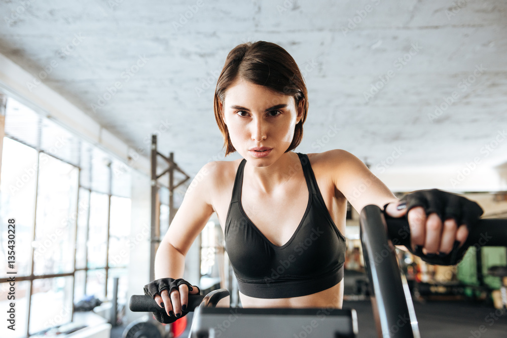 Fototapeta premium Beautiful young sportswoman training on stationary bike in gym