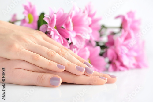 Hands of a woman with pink manicure on nails and pink flowers on a white background