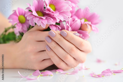 Hands of a woman with pink manicure on nails and pink flowers on a white background