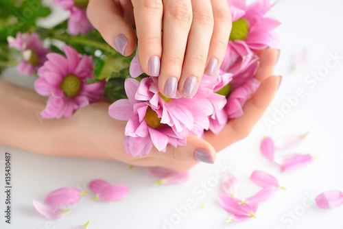 Hands of a woman with pink manicure on nails and pink flowers on a white background