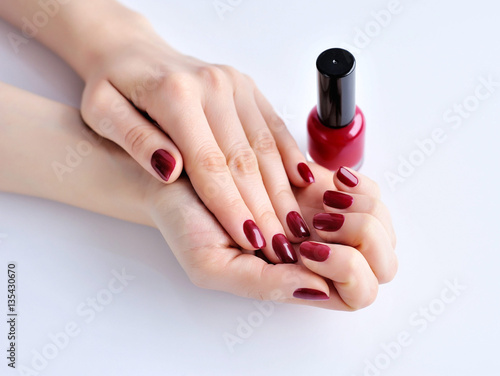 Hands of a woman with dark red manicure and nail polish bottle