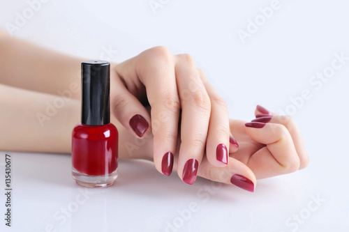 Hands of a woman with dark red manicure and nail polish bottle