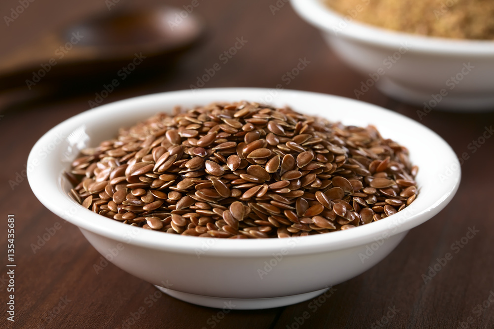 Brown flax seeds or linseeds in small bowl, photographed on dark wood with natural light (Selective Focus, Focus one third into the seeds) Brown flax seeds or linseeds in small bowl, photographed on dark wood with natural light (Selective Focus, Focus one third into the seeds)