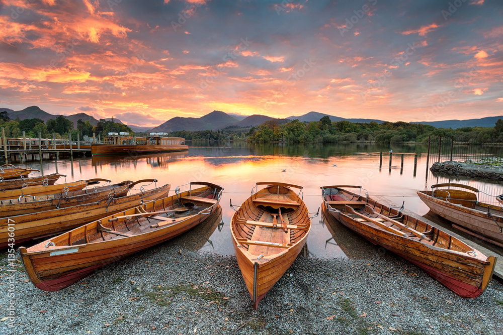 Fototapeta premium A fiery sunset over boats on the shore of Derwentwater at Keswick in the Lake District in Cumbria