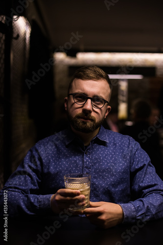 Business man, in blue shirt and glasses, drinking cocktail of vintage old fashion glass in loft bar