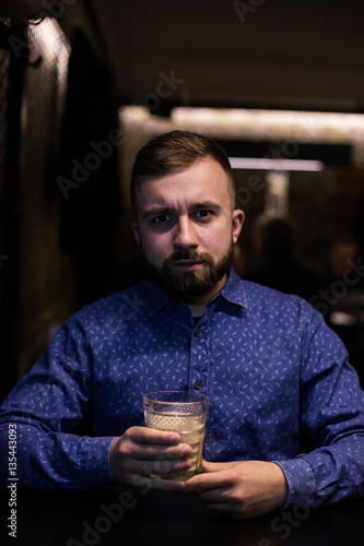 Business man, in blue shirt and glasses, drinking cocktail of vintage old fashion glass in loft bar