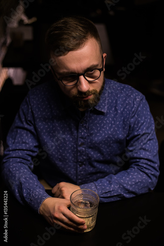 Business man, in blue shirt and glasses, drinking cocktail of vintage old fashion glass in loft bar