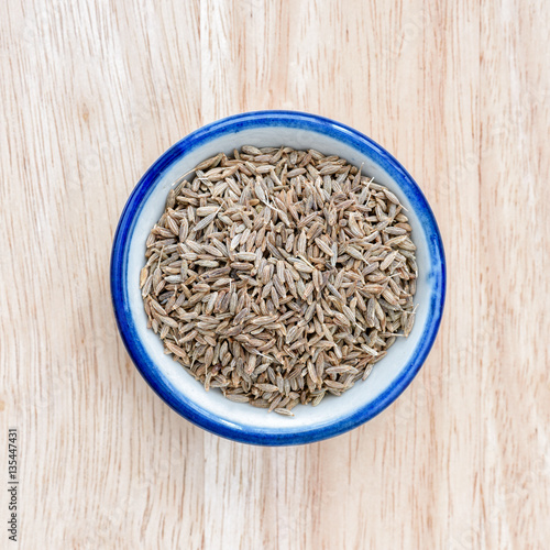 Fennel seed in bowl on wood floor background.