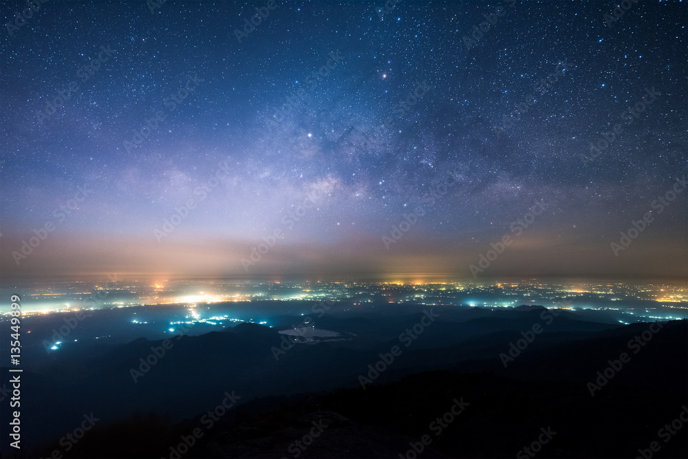 Night landscape of Milky way above the light of countryside area and mountain.