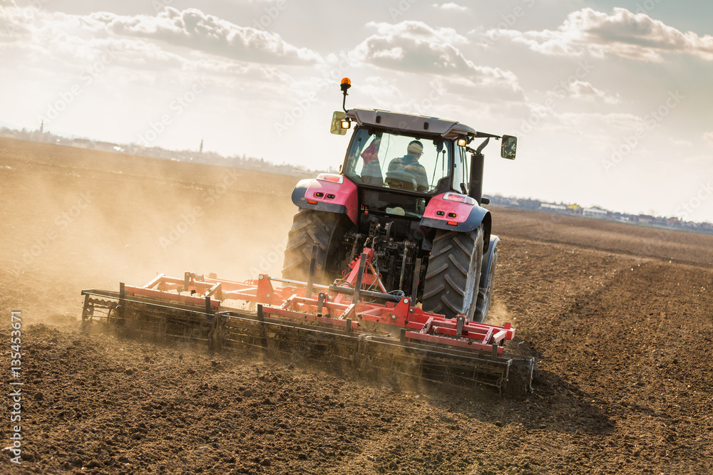 Fototapeta premium Farmer in tractor preparing land with seedbed cultivator