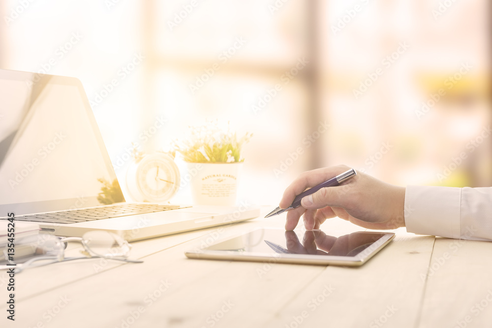 Businessman making notes on his digital tablet at the office meeting with computer laptop and glasses.