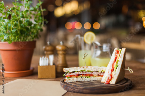Big, tasty sandwich with ham, tomato, lettuce, cheese on the wooden plate in the restaurant