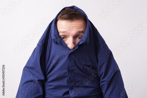 Young man hiding in a blue shirt, knitting his brows with surpri photo