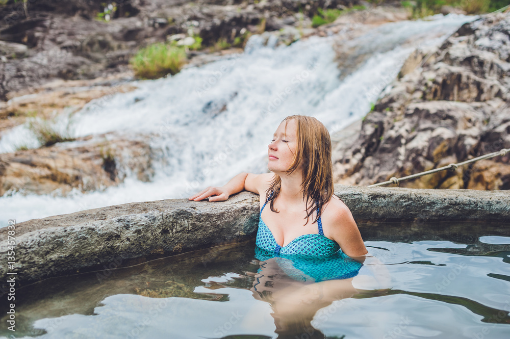 Geothermal spa. Woman relaxing in hot spring pool against the background of a waterfall