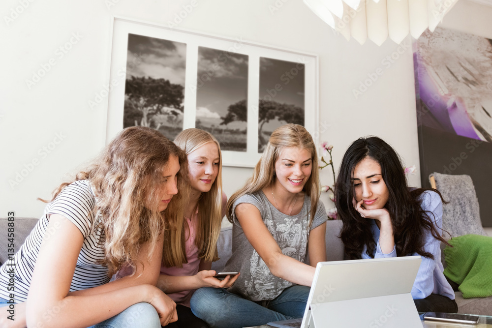 Happy teenage girls using laptop while sitting on sofa at home