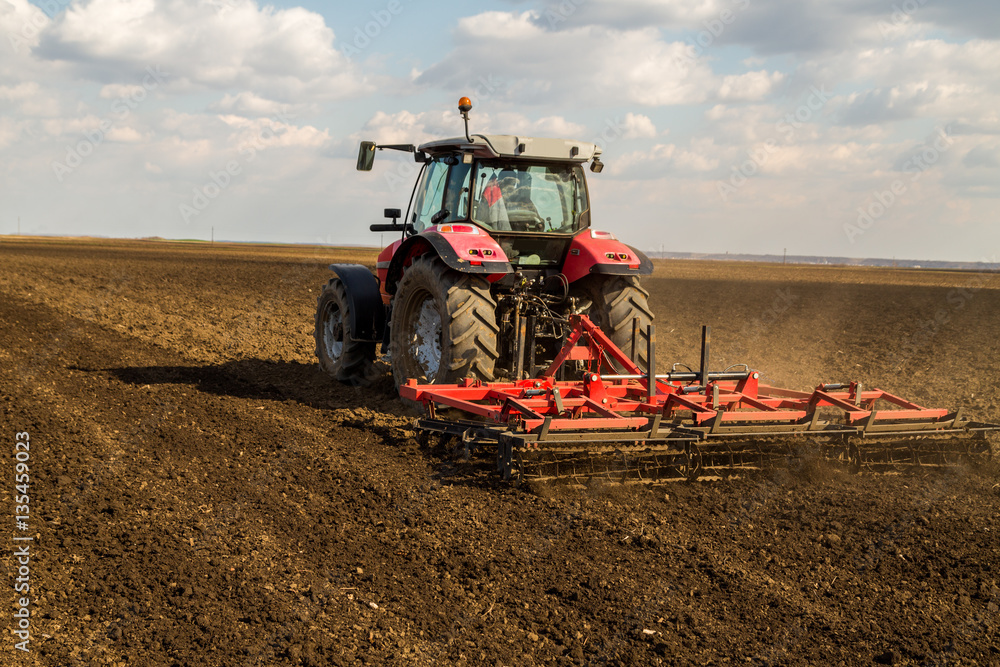Fototapeta premium Farmer in tractor preparing land with seedbed cultivator as part of pre seeding activities in early spring season of agricultural works at farmlands.