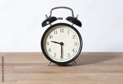 It is half past nine o'clock. The time is 9:30. Retro clock isolated on a wooden table. White background.