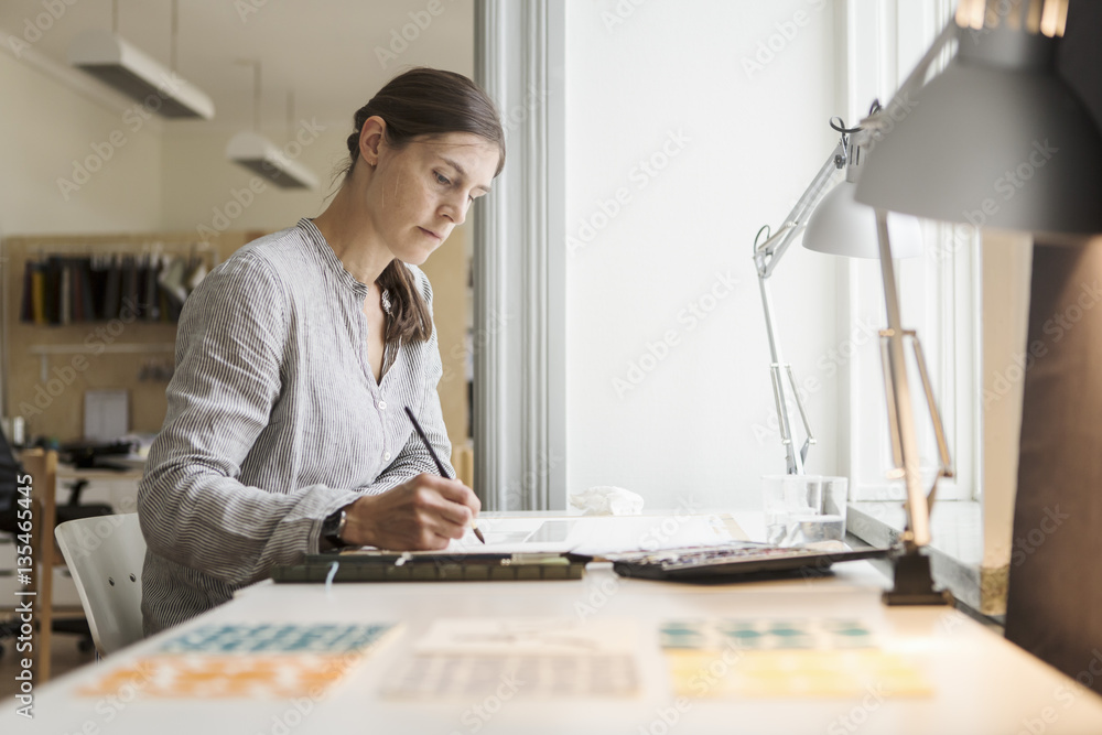 Serious woman painting while sitting at table in creative office Serious woman painting while sitting at table in creative office