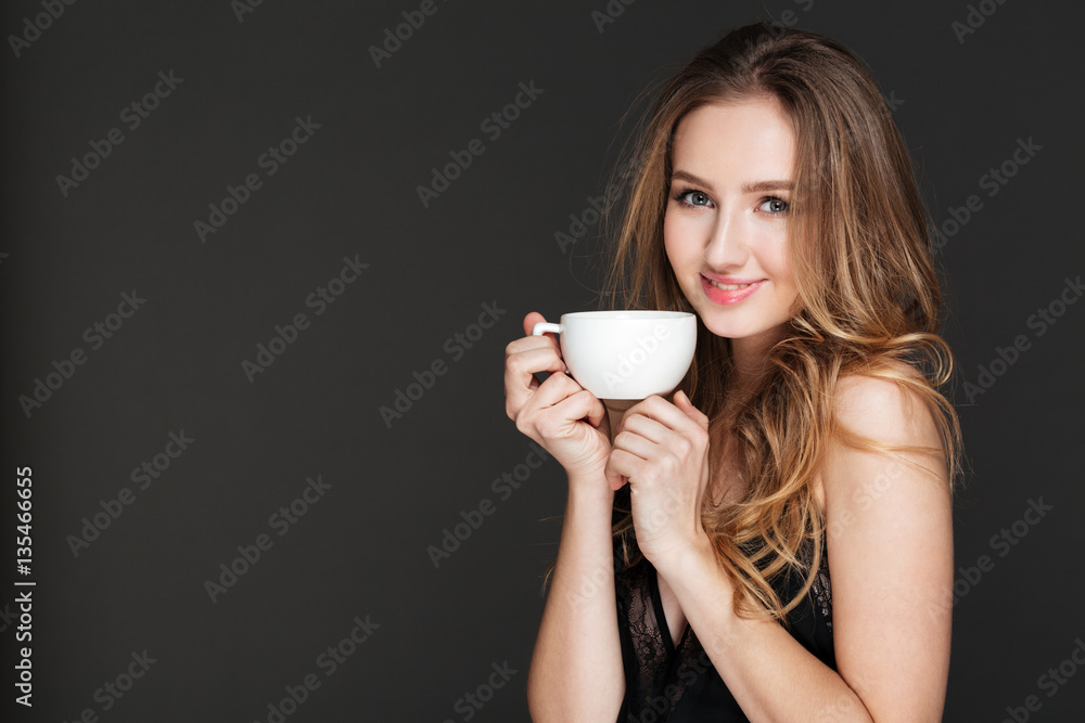 Smiling woman drinking coffee over dark background Smiling woman drinking coffee over dark background