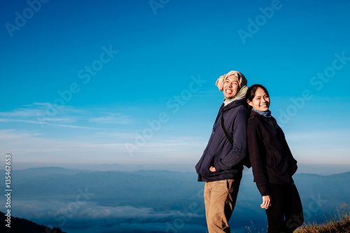young adult asian couple standing together enjoys rise to the top of the mountain with light of morning in vintage style