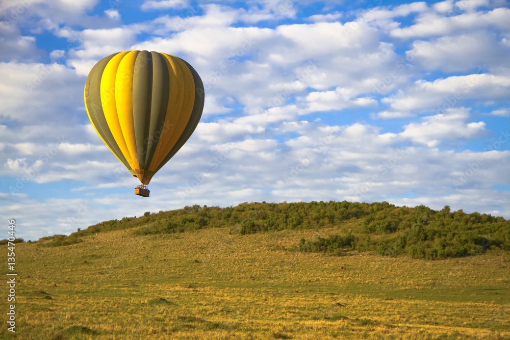 A colorful hot air balloon soars above the landscape of the Masai Mara National park in Kenya