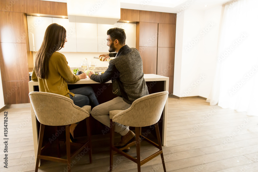 Young couple sitting in the kitchen with his back and drinking w Young couple sitting in the kitchen with his back and drinking w