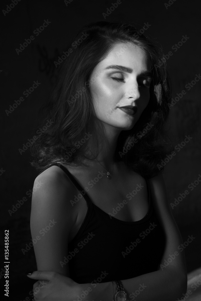 Black and white portrait of a girl in a black hat looking away. Beautiful with bright makeup. The girl in the rays of the sun. Black and white portrait of a girl in a black hat looking away. Beautiful with bright makeup. The girl in the rays of the sun.
