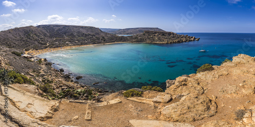 Malta - Panoramic view of Ghajn Tuffieha sandy beach with sail boat  blue sky and crystal clear green sea water 