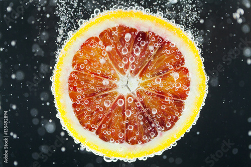 Fotografi Orange citrus slice falling into water