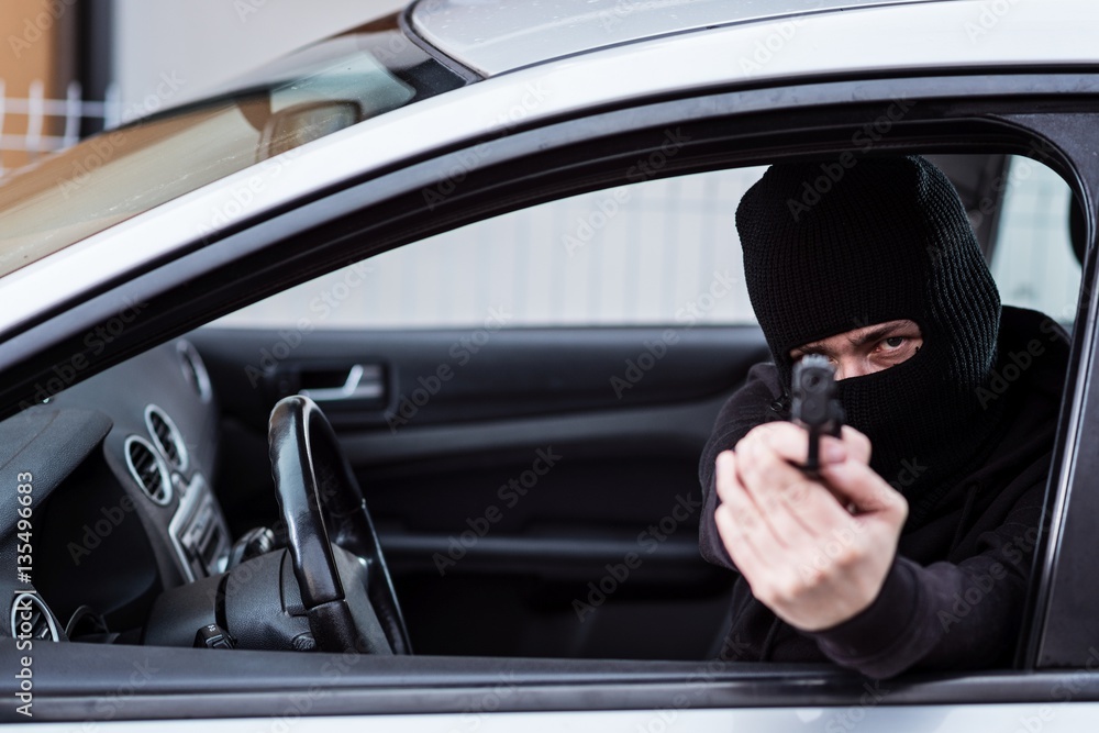 Man in black balaclava with handgun driving a car.