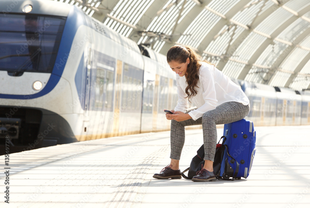 happy woman sitting on suitcase using mobile phone