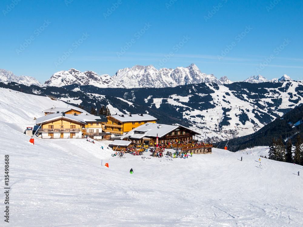 Downhill slope and apres ski mountain hut with restaurant terrace in Saalbach Hinterglemm Leogang winter resort, Tirol, Austria, Europe. Sunny day shot. Downhill slope and apres ski mountain hut with restaurant terrace in Saalbach Hinterglemm Leogang winter resort, Tirol, Austria, Europe. Sunny day shot.